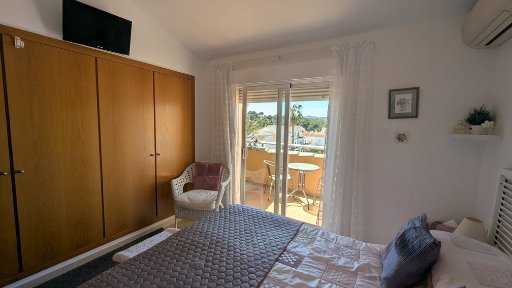 Chambre principale avec grand placard intégré en bois, climatisation et accès à une terrasse privée offrant une vue dégagée sur les environs.