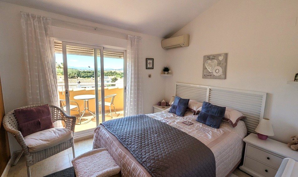 Chambre principale lumineuse avec plafond incliné, disposant d'une terrasse privée offrant une vue dégagée, de la climatisation et d'un mobilier blanc.