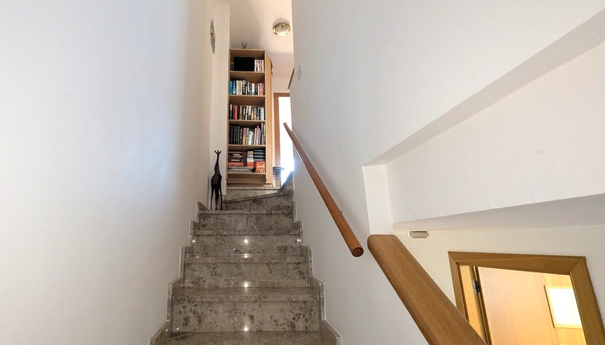 Escalier intérieur en marbre avec main courante en bois menant à l'étage, doté d'une bibliothèque encastrée et de murs blancs épurés.