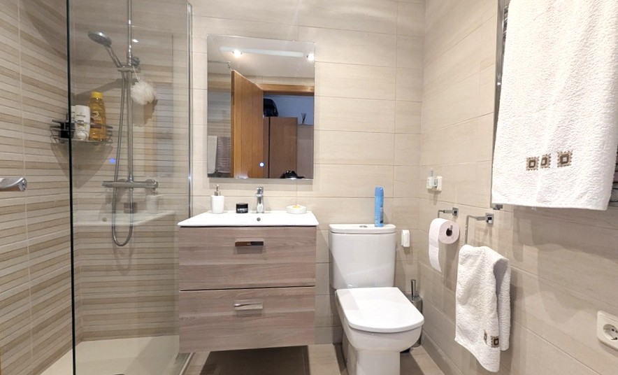 Salle de douche moderne avec paroi vitrée, meuble vasque suspendu en bois clair et carrelage mural aux tons beiges horizontaux.