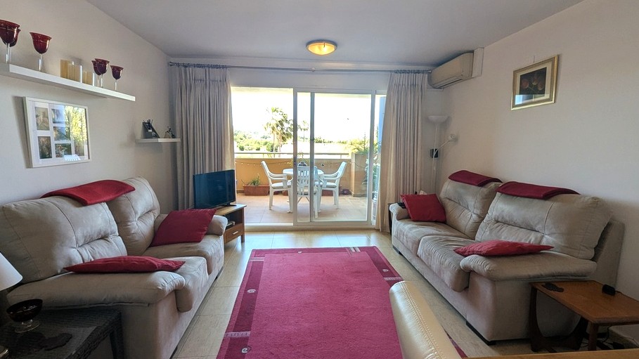 Salon lumineux avec carrelage neutre, canapés confortables et accès par baie vitrée à une terrasse meublée offrant une vue sur la végétation environnante.