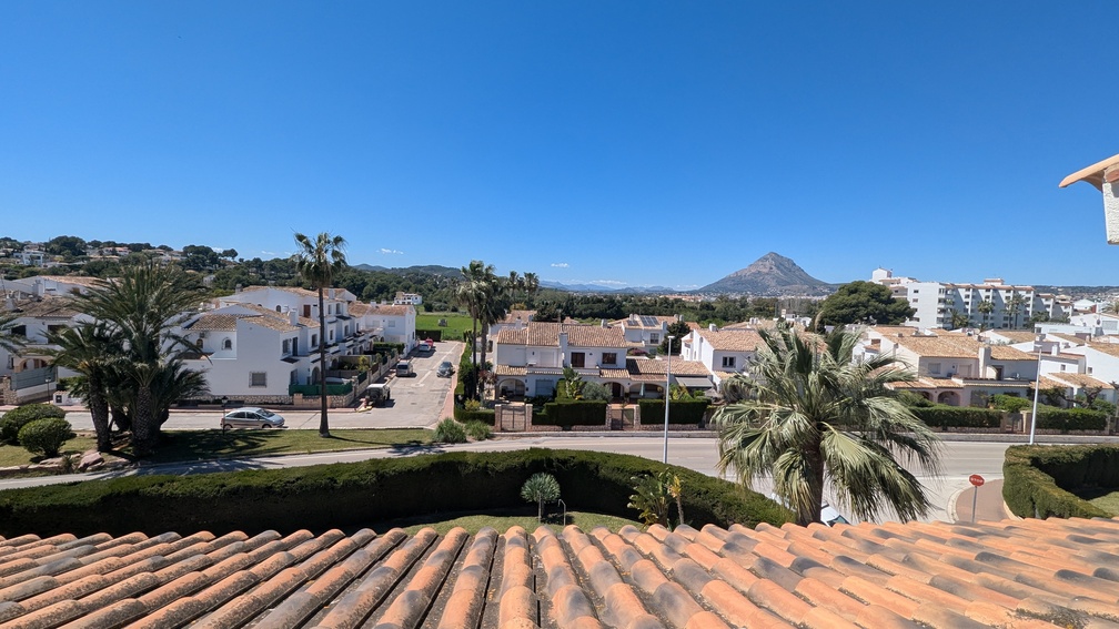 Vue dégagée depuis la terrasse sur les toits en tuiles, le quartier résidentiel environnant et la silhouette du mont Montgó se détachant à l'horizon.