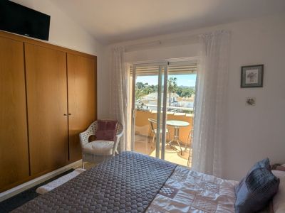 Chambre avec armoire en bois intégrée et accès à un balcon privé, offrant des vues sur les toits, les palmiers et les collines lointaines depuis son petit coin salon.