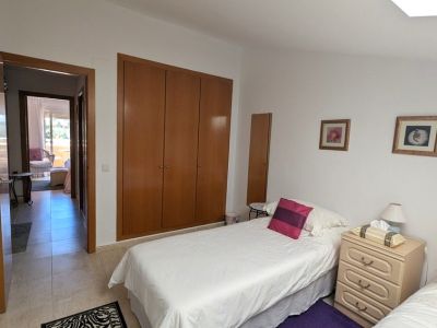 Chambre avec deux lits simples, une armoire encastrée en bois et une table de chevet. Une porte ouverte donne sur une terrasse extérieure.