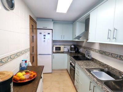 Cuisine fonctionnelle en couloir avec des armoires bleu clair, des plans de travail en granit moucheté et des murs carrelés blancs avec une frise décorative. Équipée de plaques de cuisson, four et évier.