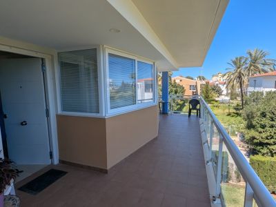 Grande terrasse privée avec carrelage marron, balustrade en verre et section vitrée. Vues sur les palmiers et le paysage résidentiel environnant.