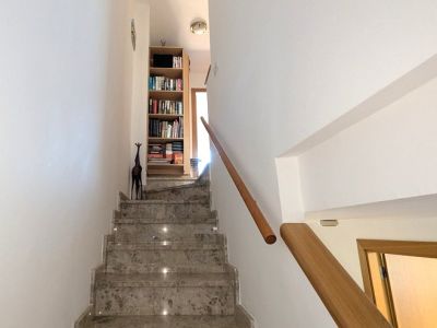L'escalier intérieur élégant présente des marches en marbre poli avec éclairage intégré et une rampe en bois chaleureux, menant à l'étage supérieur avec une bibliothèque.