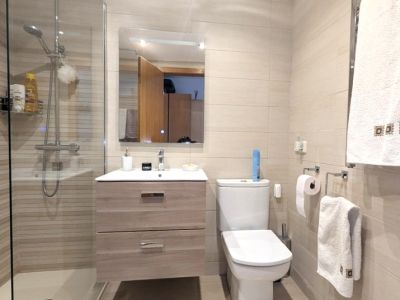 Salle de bain moderne avec douche à l'italienne vitrée et carrelage beige rayé. Elle dispose d'un meuble vasque suspendu à deux tiroirs et d'un miroir éclairé.