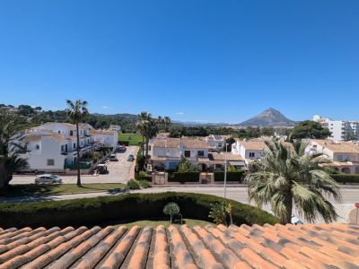 Vue panoramique depuis la terrasse, présentant des toits en terre cuite, des rues résidentielles, des palmiers luxuriants et le majestueux Montgó sous un ciel bleu dégagé.