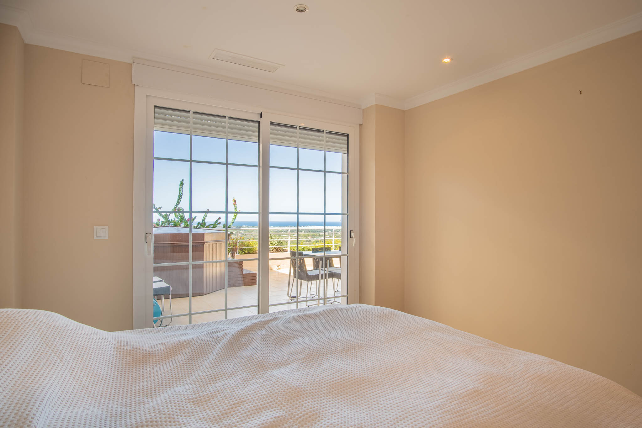 Chambre avec accès direct à la terrasse par des baies vitrées. L'espace extérieur dispose d'un jacuzzi privé et offre une vue panoramique sur la mer.