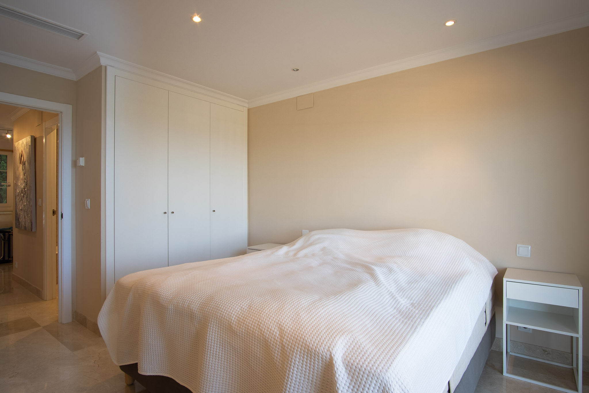 Chambre avec sol en marbre, placards intégrés blancs et éclairage par spots encastrés au plafond, offrant un design sobre et une atmosphère sereine.