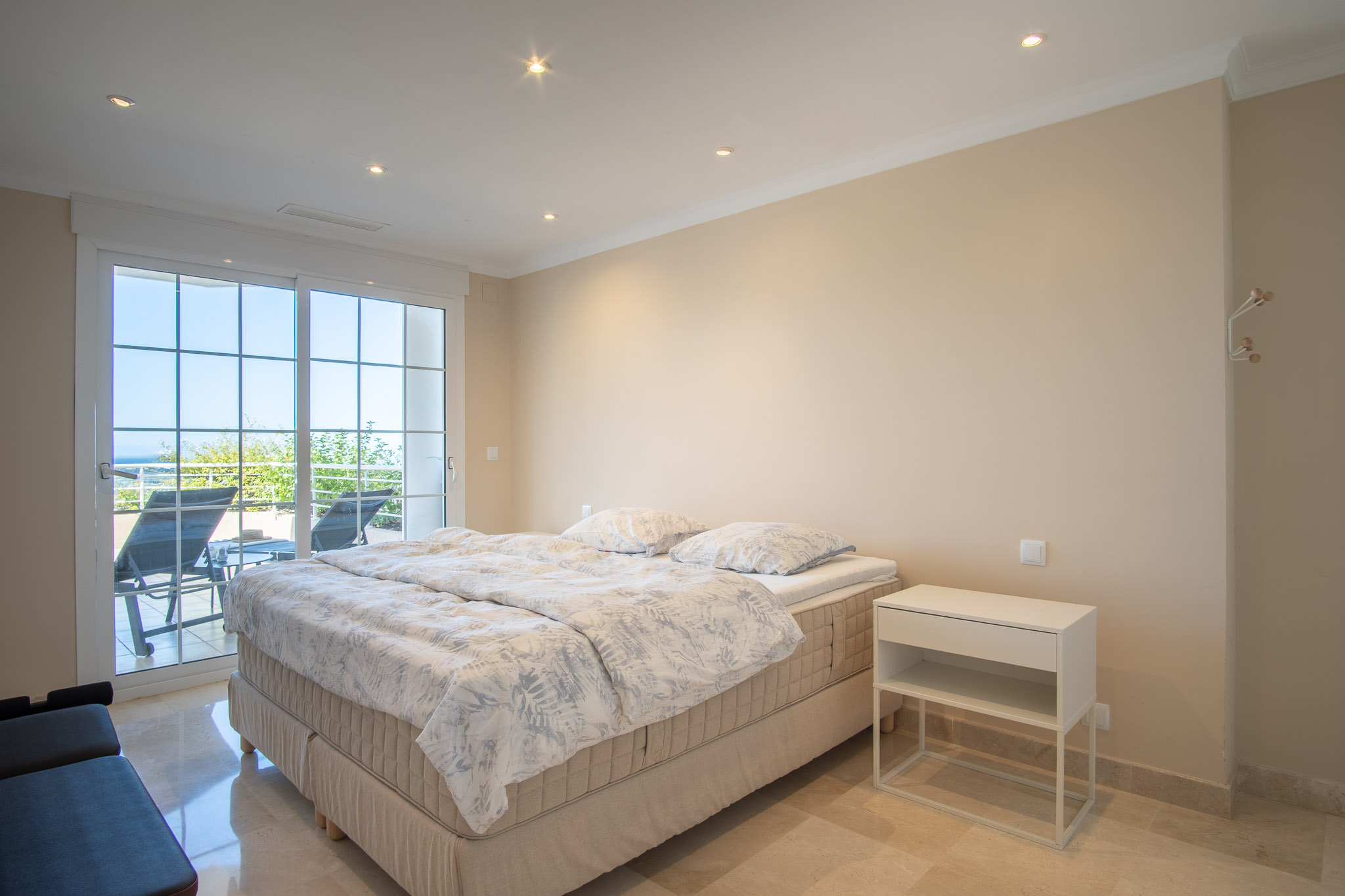Chambre avec sols en marbre et éclairage encastré. Les grandes baies vitrées offrent un accès direct à la terrasse équipée de bains de soleil face à la mer.
