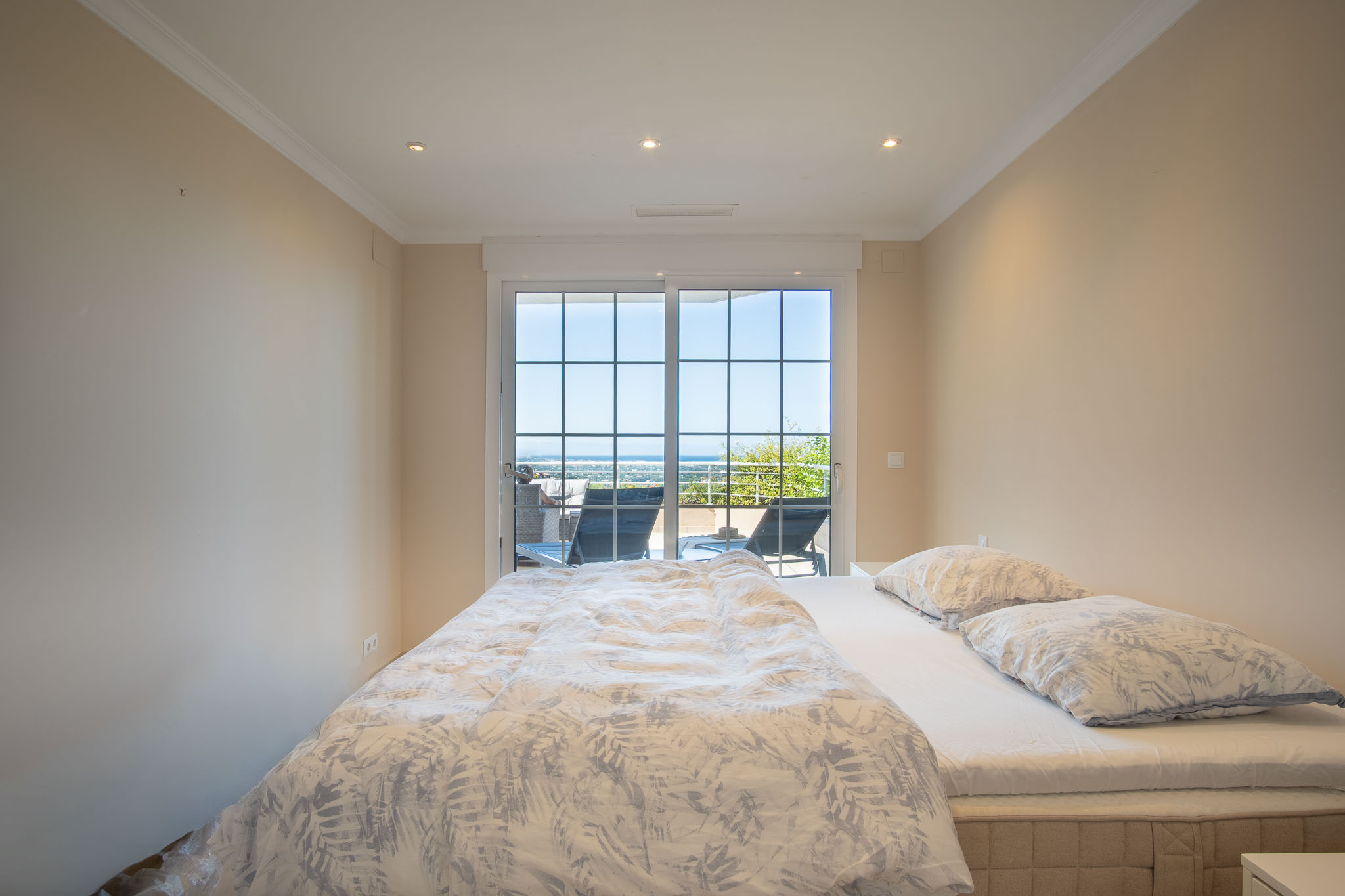 Chambre double avec accès direct à la terrasse par des portes vitrées à petits bois, offrant une vue dégagée sur la mer et un éclairage encastré.
