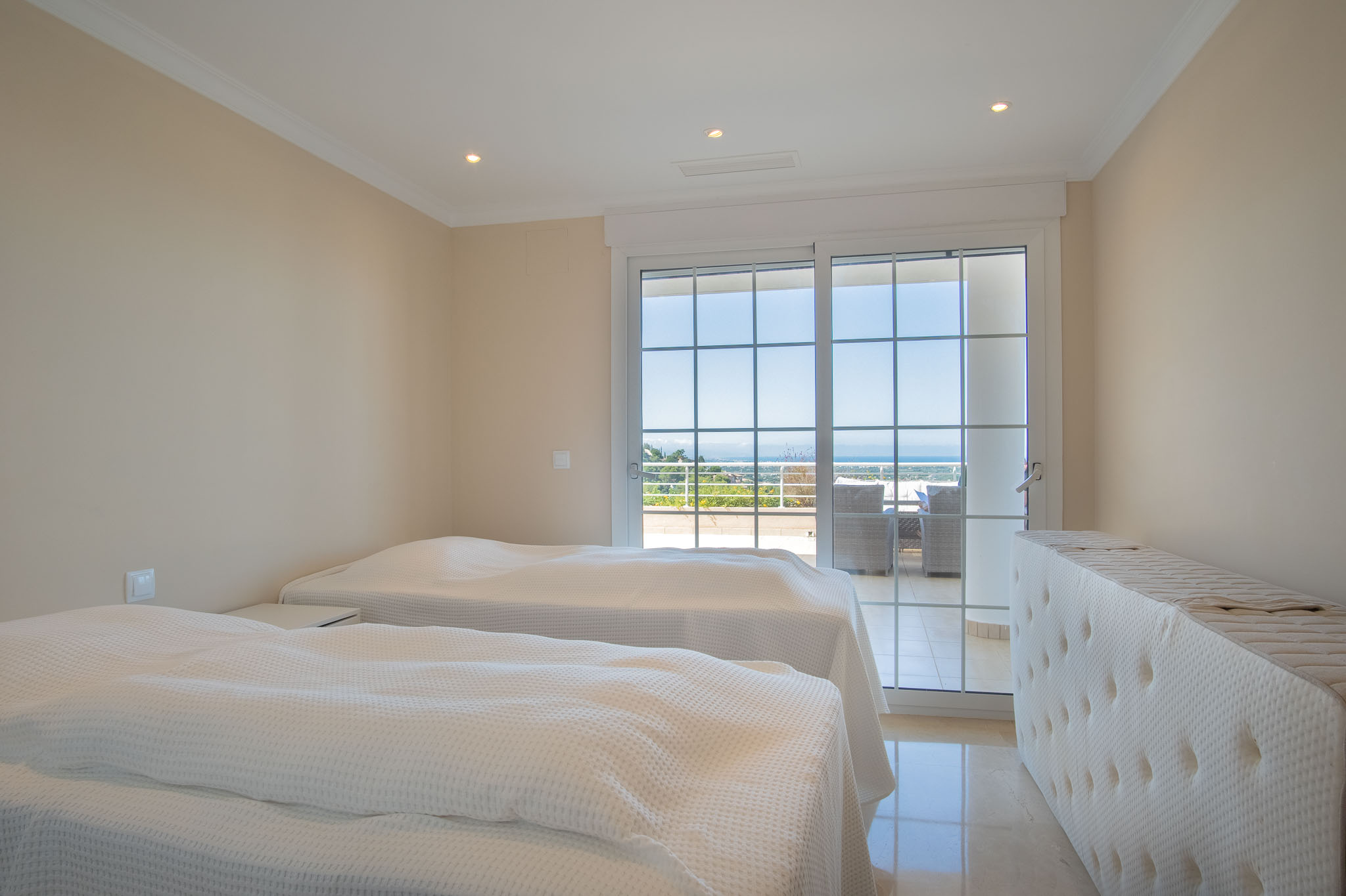 Chambre double avec sol en marbre et accès direct à la terrasse par une baie vitrée à croisillons, offrant une vue panoramique sur la mer.