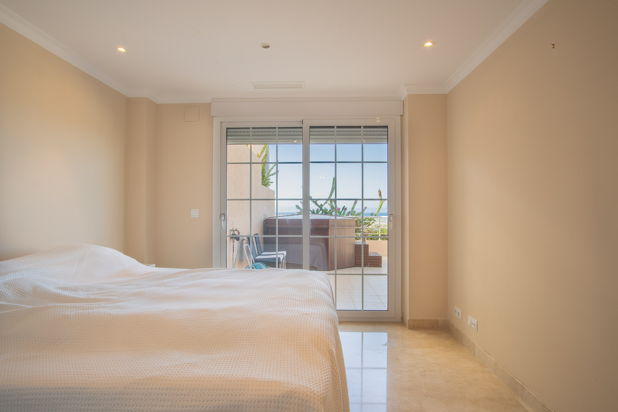Chambre lumineuse avec sol en marbre et accès direct à une terrasse privée équipée d'un jacuzzi offrant une vue sur la mer.