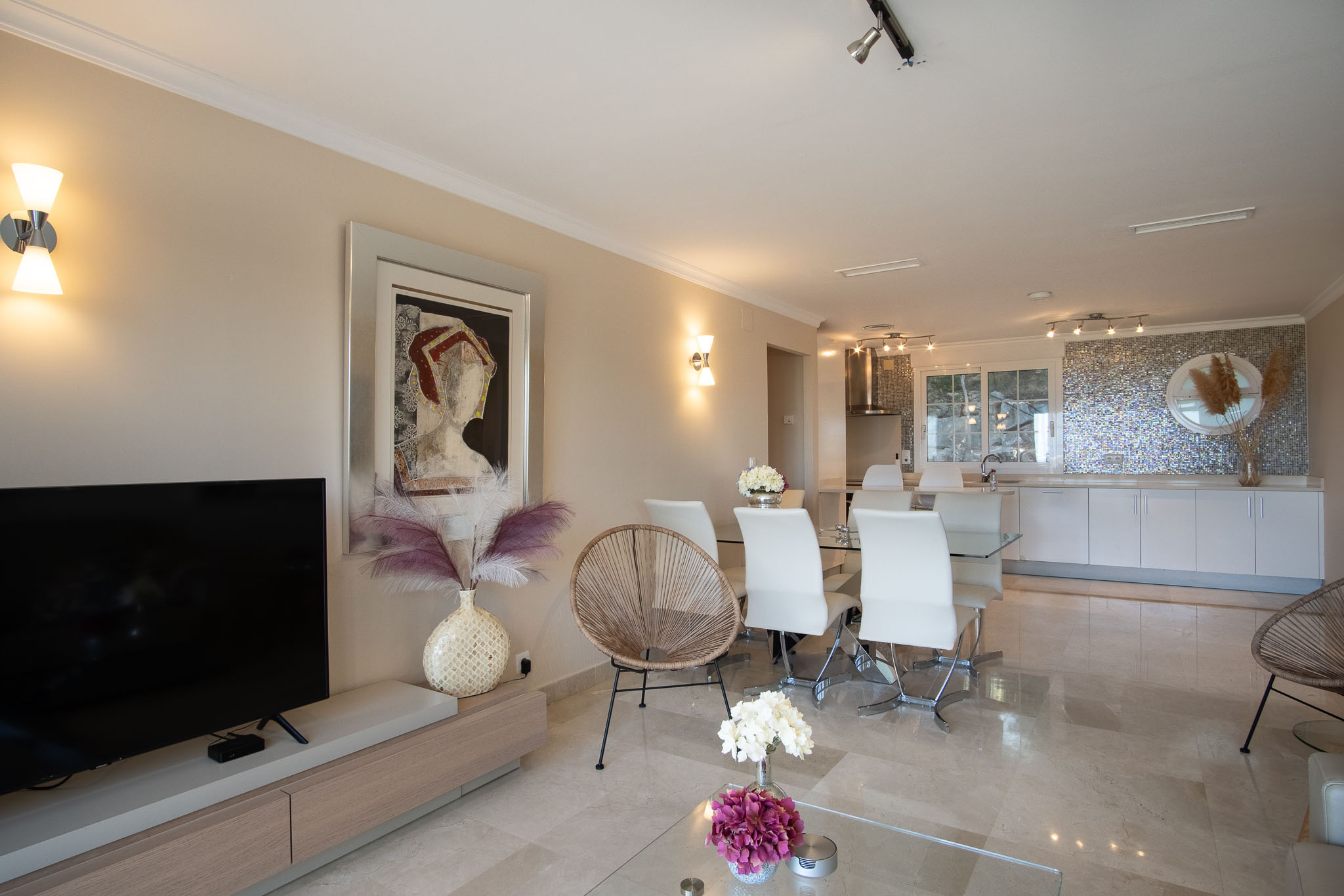 Espace de vie ouvert avec sols en marbre poli, mobilier moderne et cuisine intégrée dotée d'une crédence en mosaïque irisée distinctive.