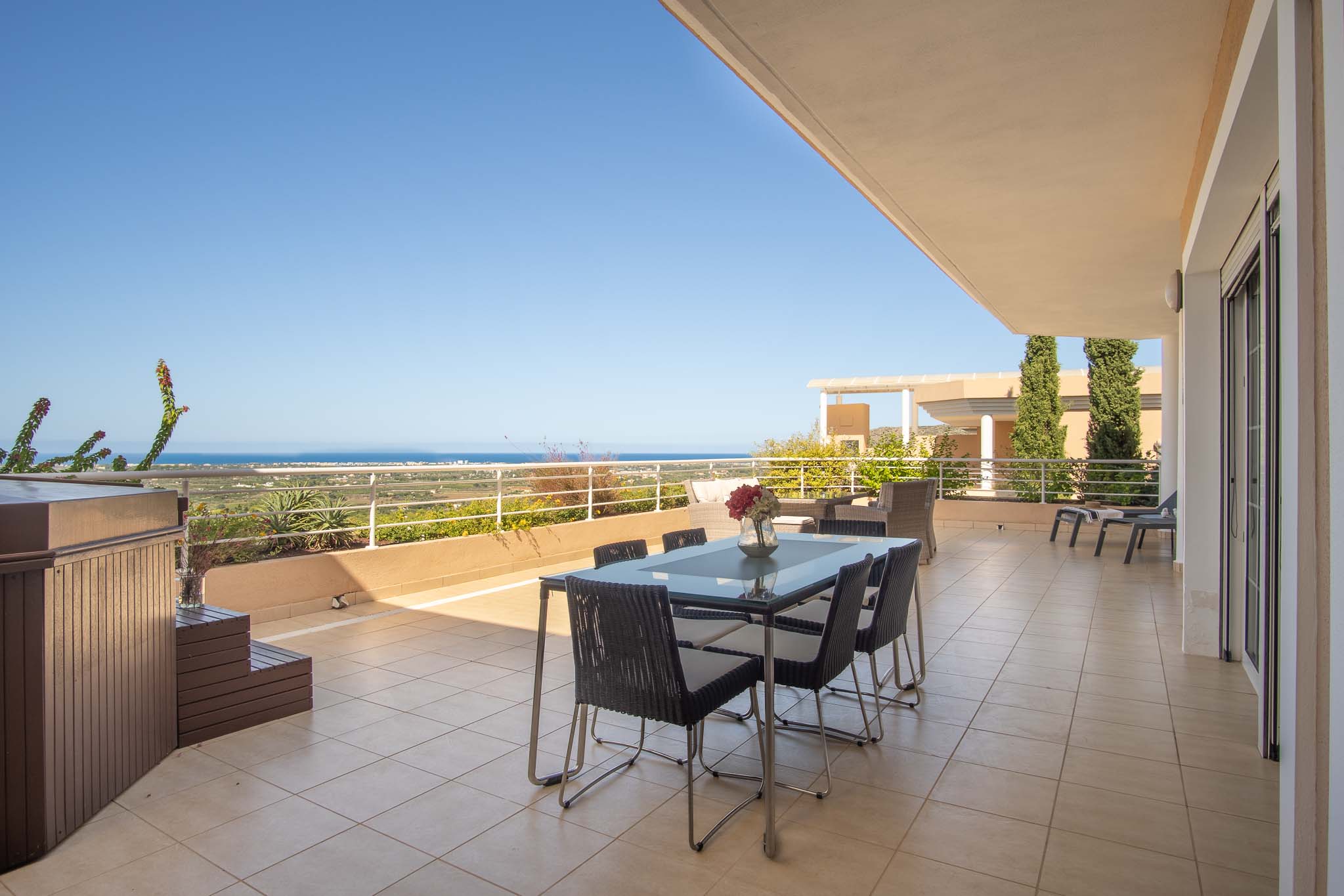 Grande terrasse avec jacuzzi privé, coin repas extérieur et vues panoramiques sur la mer Méditerranée. Le sol est en grès cérame avec une rambarde de sécurité blanche.