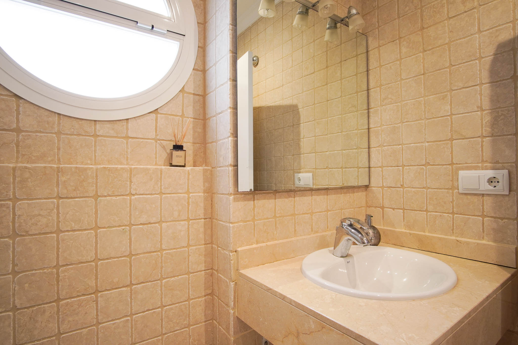 Salle de bain avec murs en marbre vieilli, plan de vasque en pierre naturelle et une fenêtre circulaire distinctive laissant entrer la lumière.