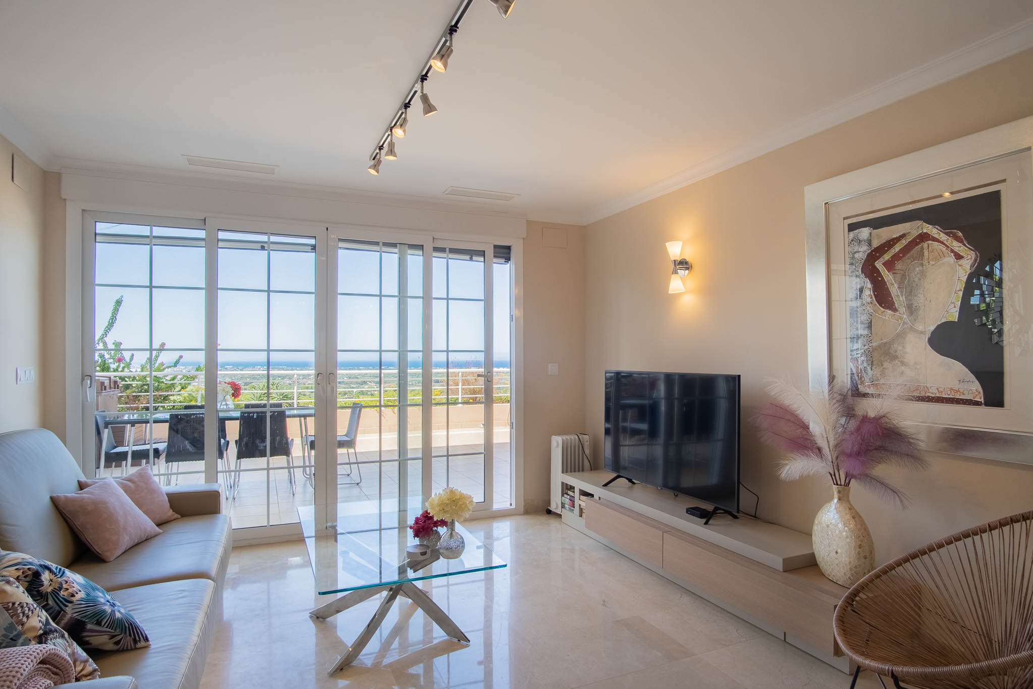 Salon lumineux avec sol en marbre, mobilier moderne et grandes baies vitrées s'ouvrant sur une terrasse offrant une vue panoramique sur la mer.