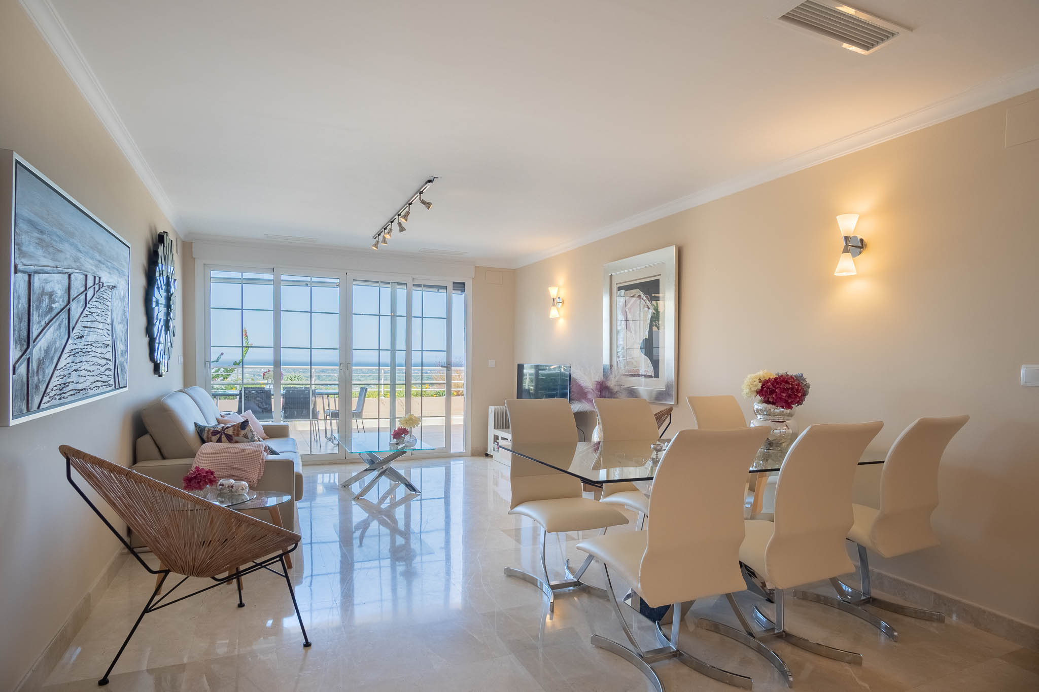 Salon-salle à manger avec sols en marbre poli, mobilier moderne en verre et grandes baies vitrées offrant une vue sur la mer et un accès direct à la terrasse.