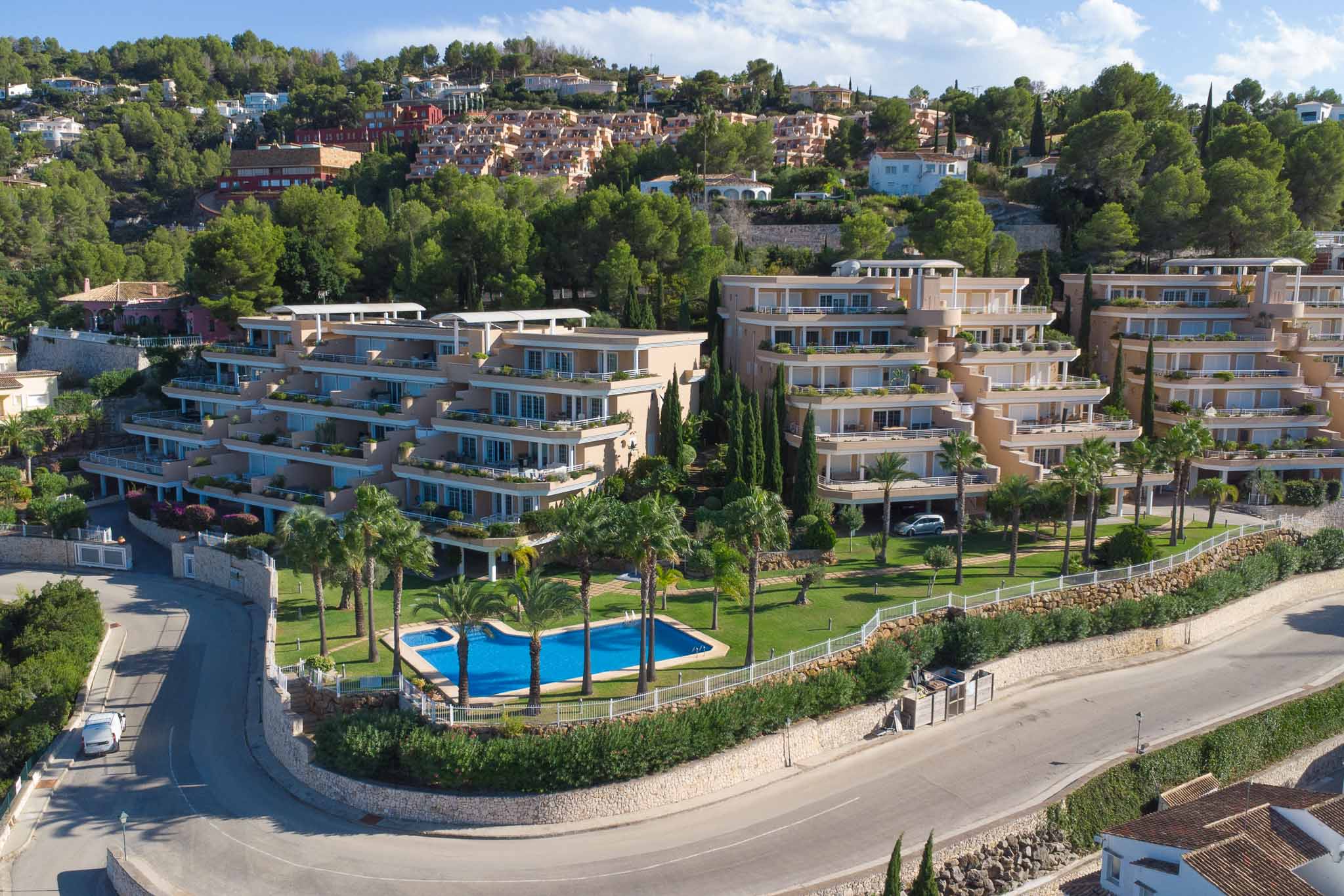 Vue aérienne du complexe Las Mimosas à La Sella, mettant en avant son architecture en terrasses, sa piscine communautaire bordée de palmiers et ses jardins.