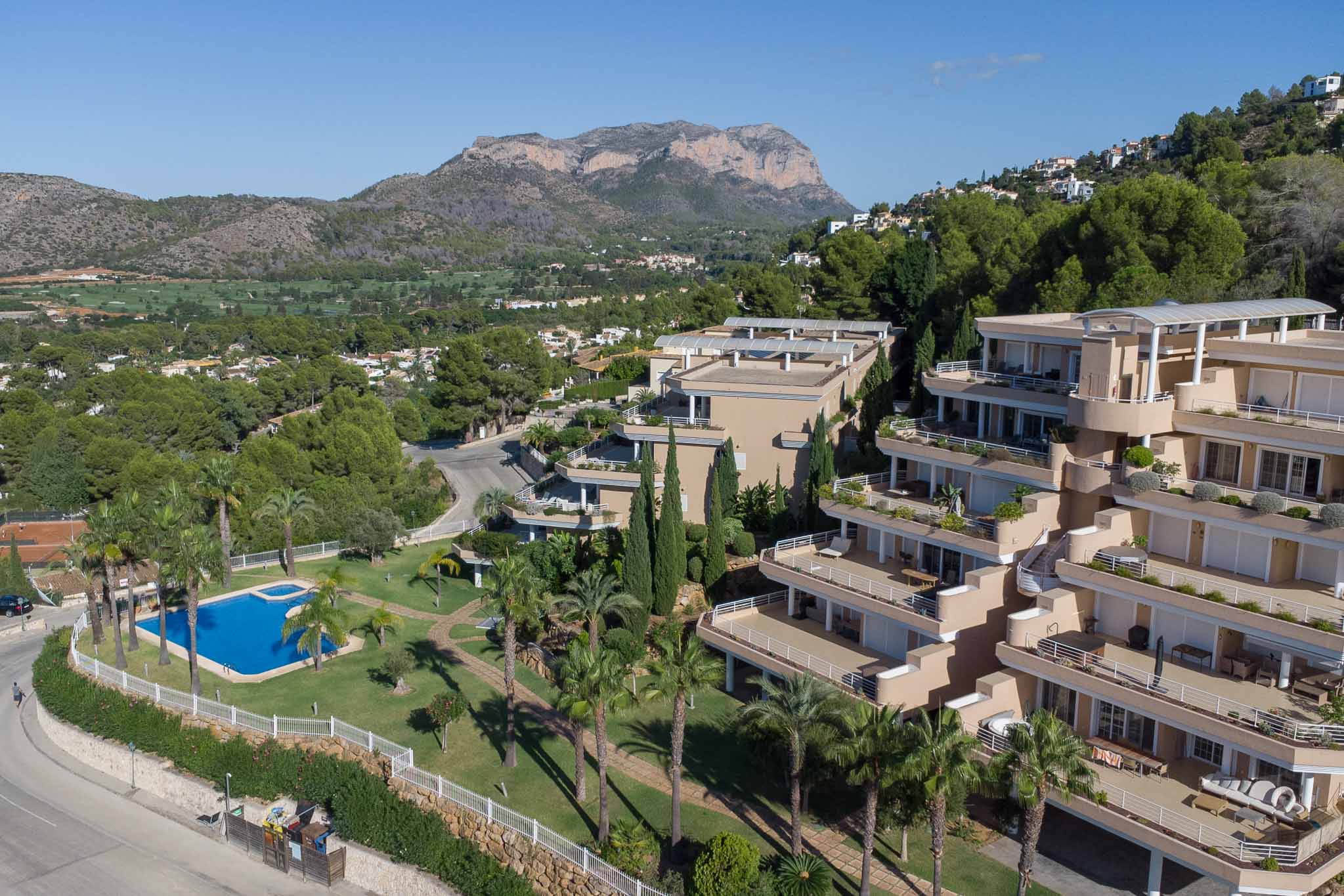 Vue aérienne du complexe Las Mimosas, illustrant la piscine commune, les jardins méditerranéens et les bâtiments en terrasses face au golf et au Montgó.