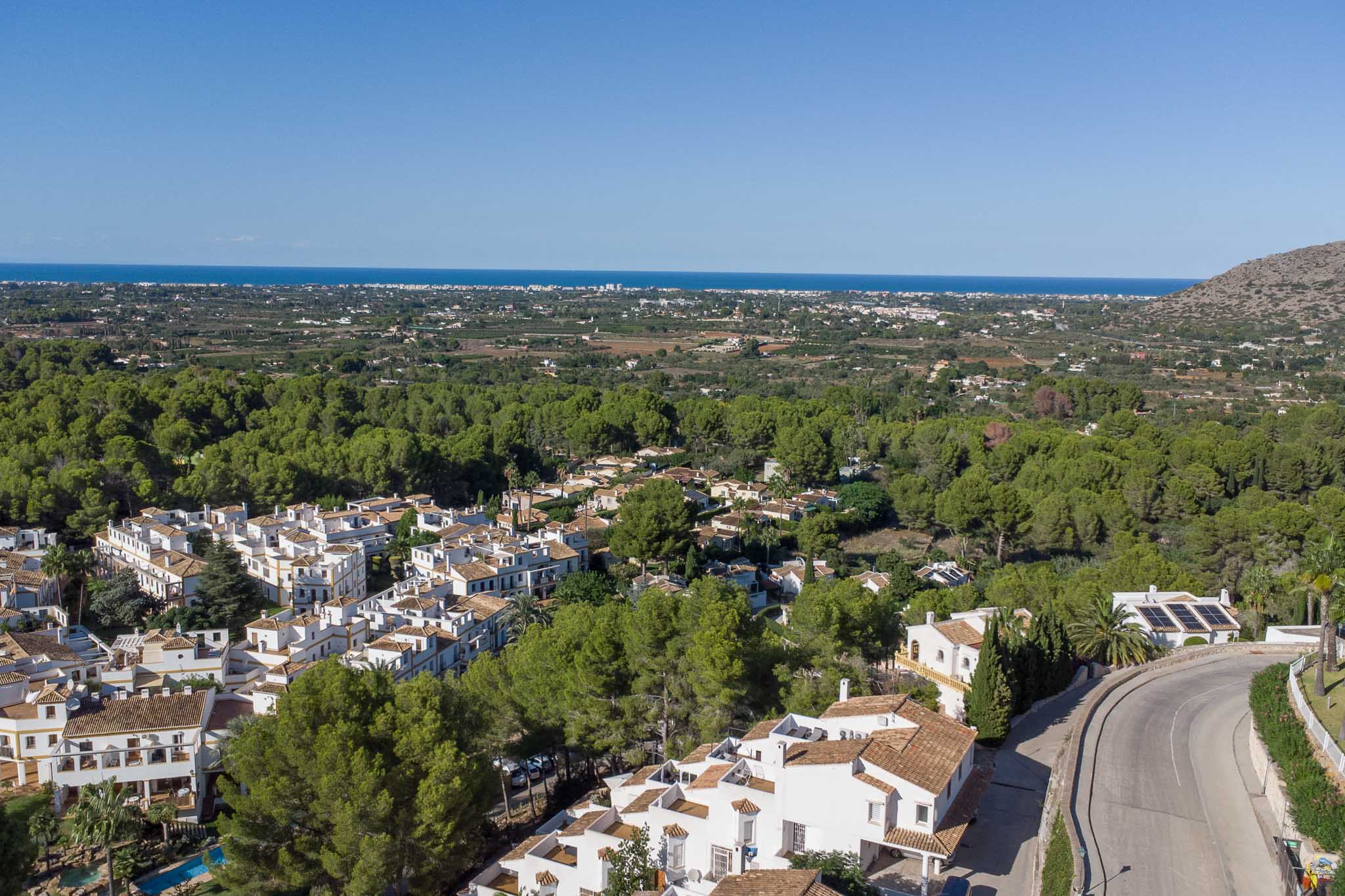 Vue aérienne panoramique du complexe Las Mimosas à La Sella, entouré d'une pinède avec la mer Méditerranée se dessinant à l'horizon.