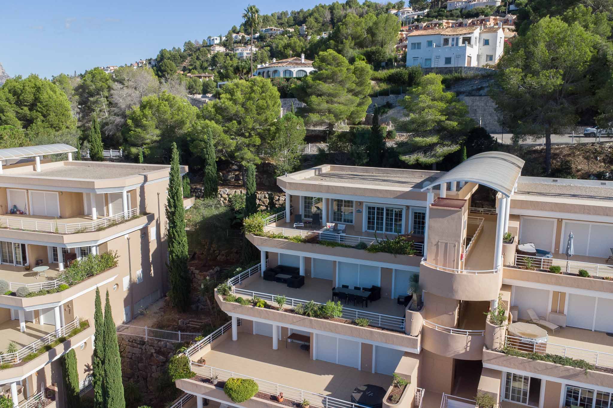 Vue extérieure du complexe Las Mimosas, illustrant l'architecture en gradins avec de vastes terrasses privées et des façades aux tons ocre intégrées à la colline boisée.