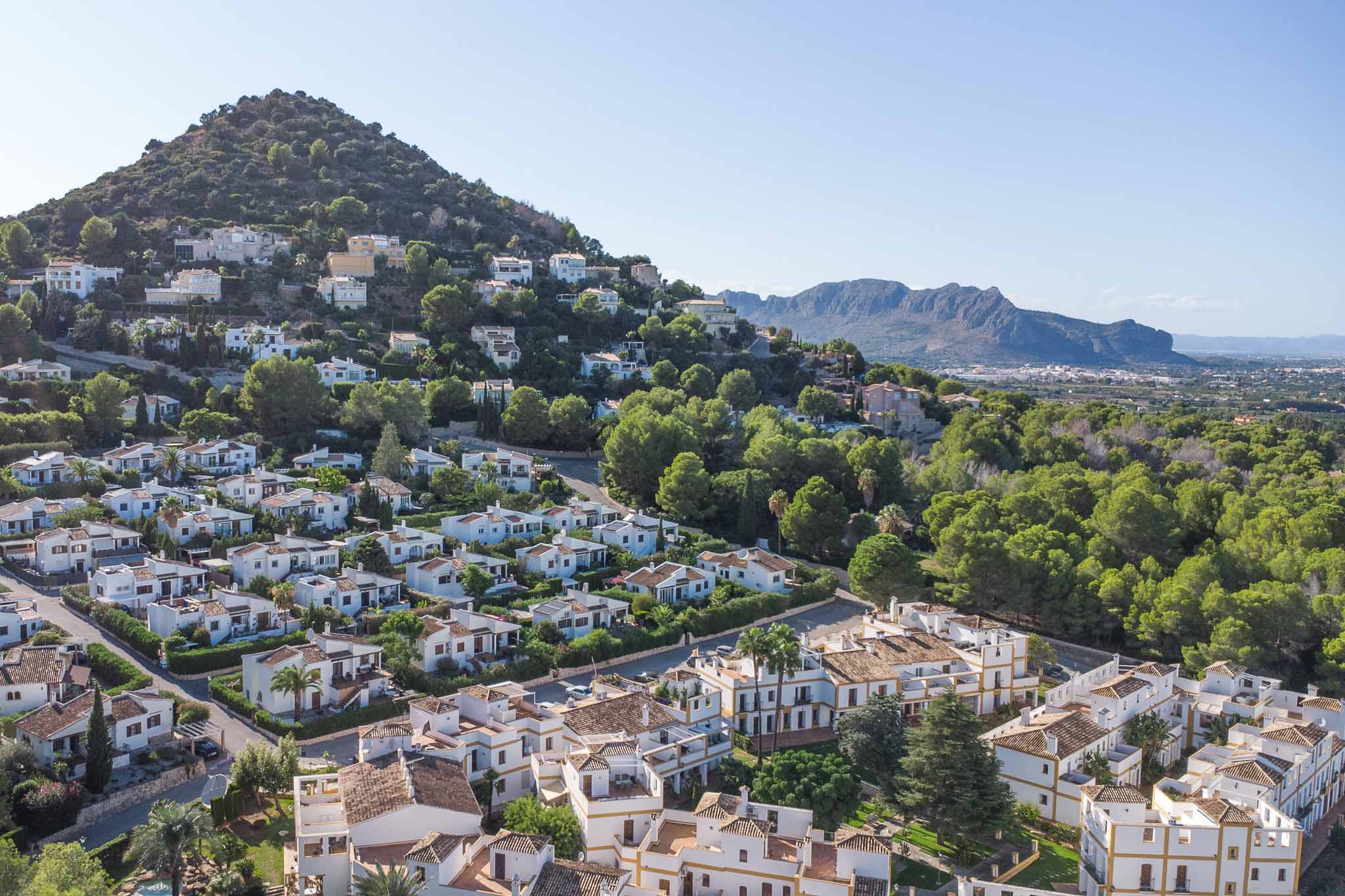 Vue panoramique sur le quartier résidentiel de La Sella, illustrant l'architecture méditerranéenne nichée dans une pinède avec les montagnes en arrière-plan.