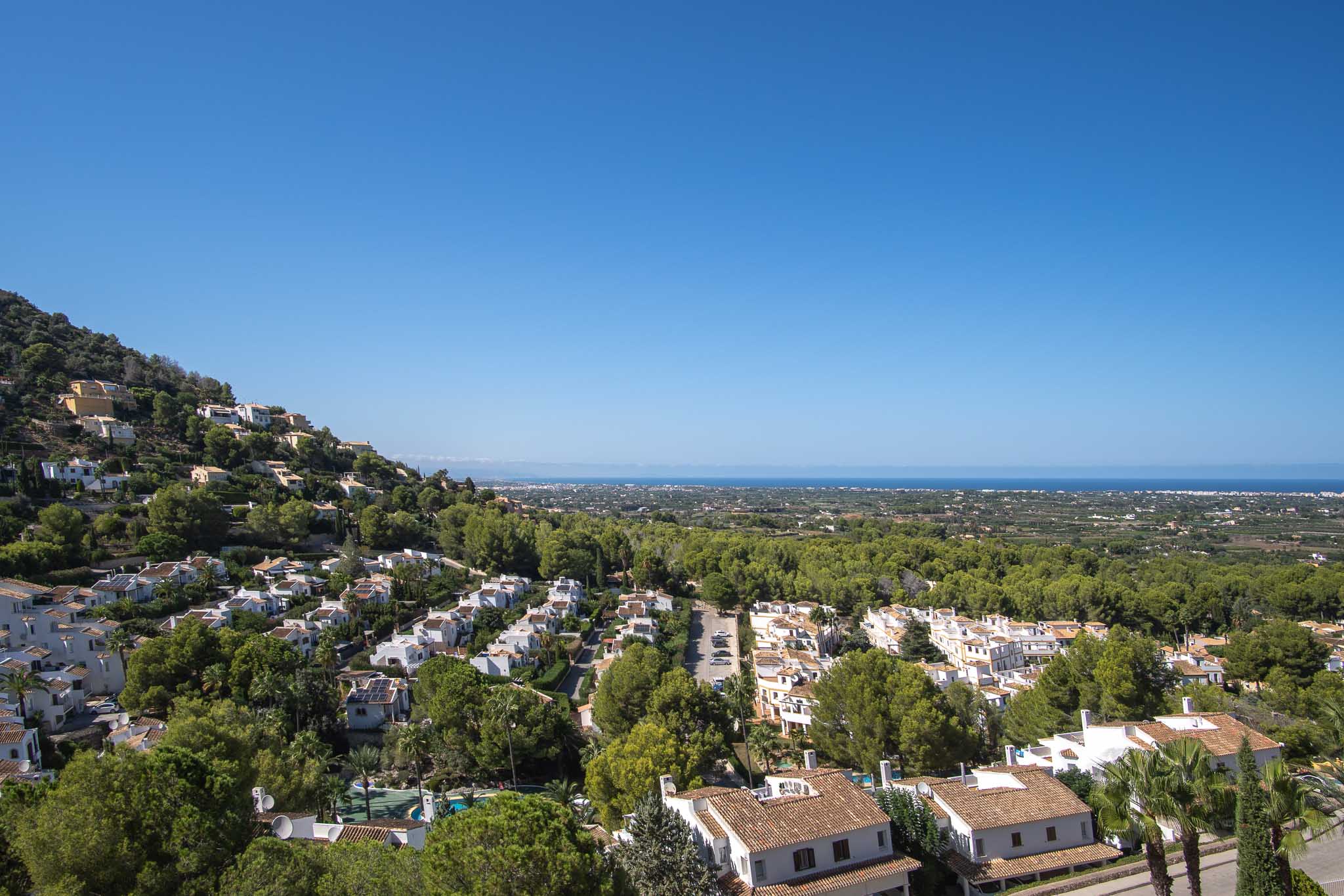 Vues panoramiques depuis La Sella vers la mer Méditerranée, illustrant l'architecture résidentielle intégrée dans un environnement verdoyant sous un ciel dégagé.