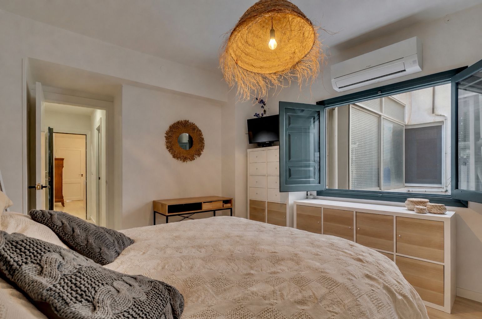 Chambre lumineuse avec lit double, fenêtre en bois bleu et lampe en osier suspendue.
