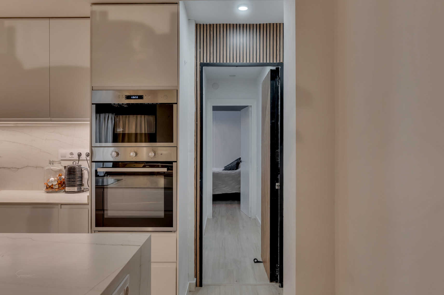 Détail de la cuisine avec four intégré et vue sur la chambre à travers une porte au design en bois.