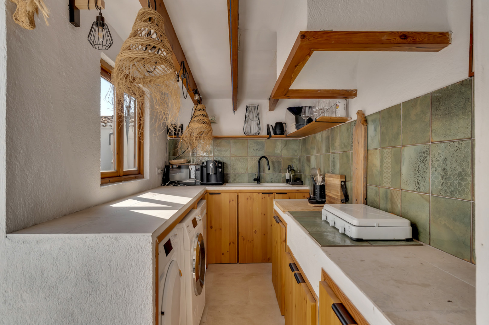 Détail de la cuisine avec meubles en bois clair, plan de travail intégré et crédence verte.