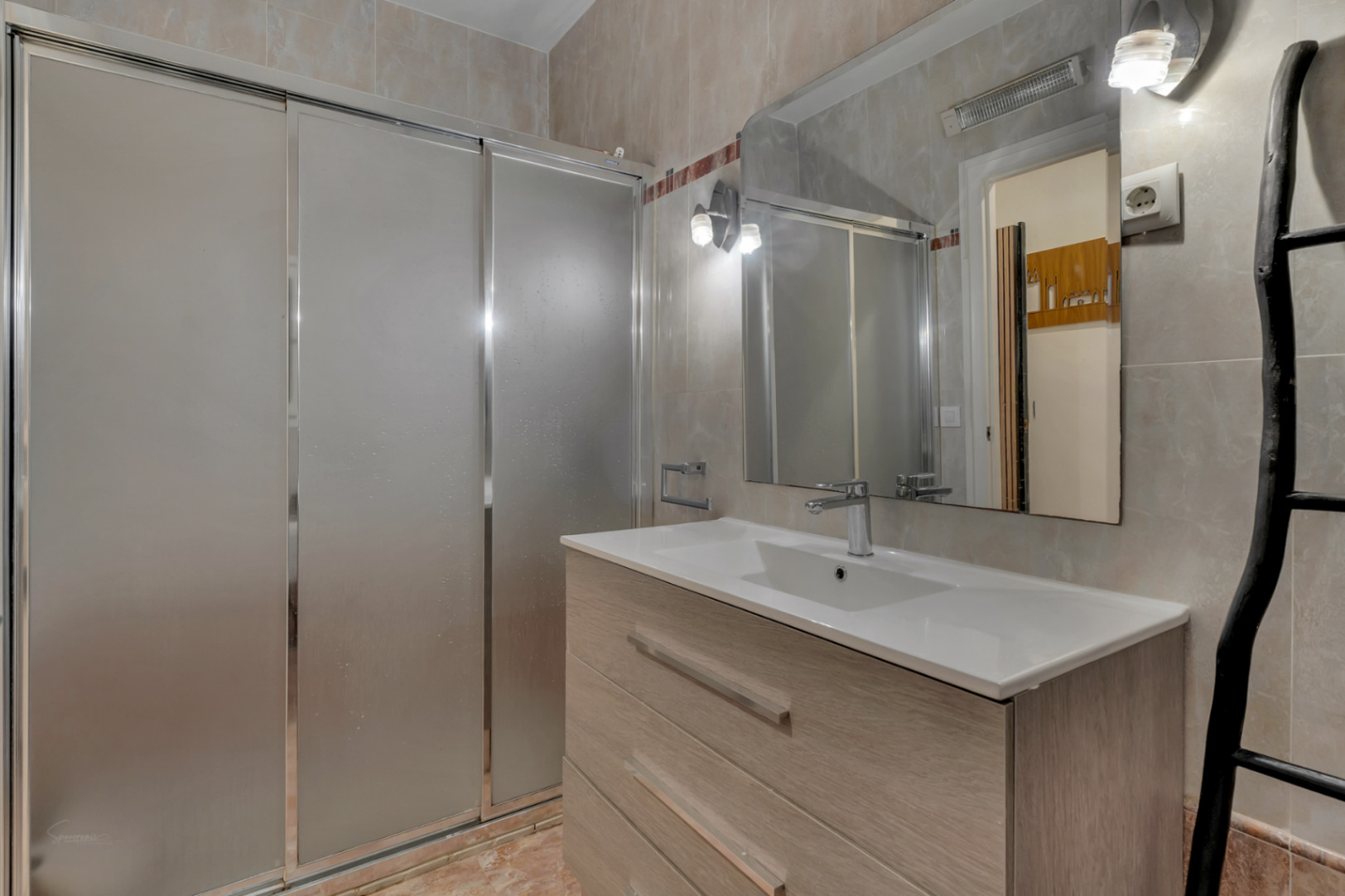Détail de la salle de bain avec douche coulissante, lavabo moderne avec meuble en bois clair et miroir éclairé.