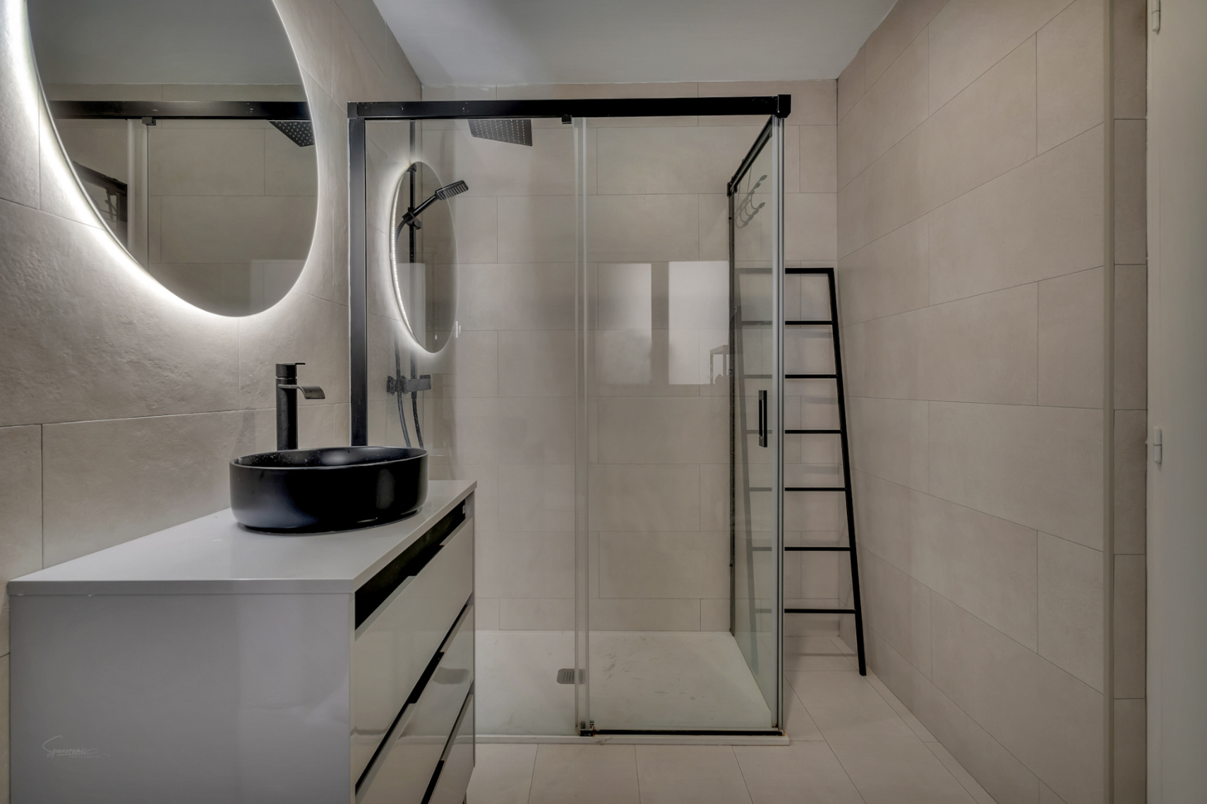 Détail de la salle de bain moderne avec lavabo noir sur comptoir blanc et douche vitrée.