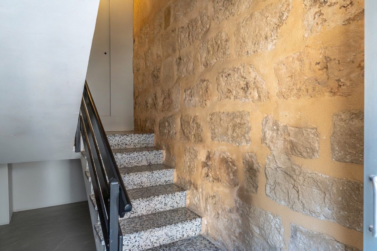 Détail de l'escalier avec mur en pierre apparente et marches en terrazzo.