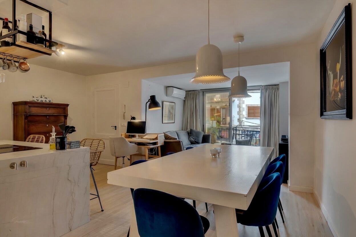 Détail du salon-salle à manger avec table blanche, chaises en velours bleu et accès à la terrasse.