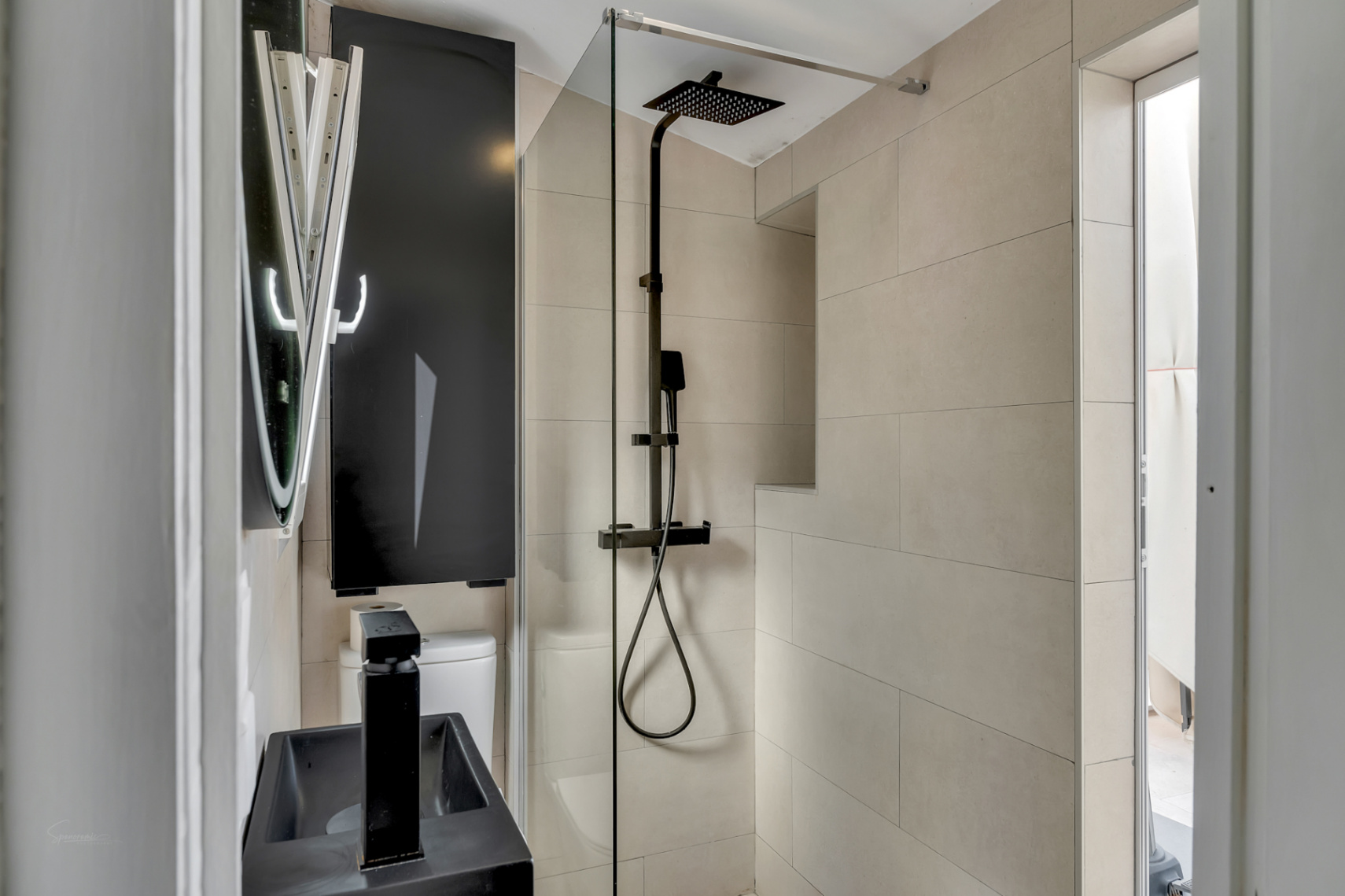 Détail d'une salle de bain moderne avec douche à effet pluie noire, lavabo noir et carrelage crème.
