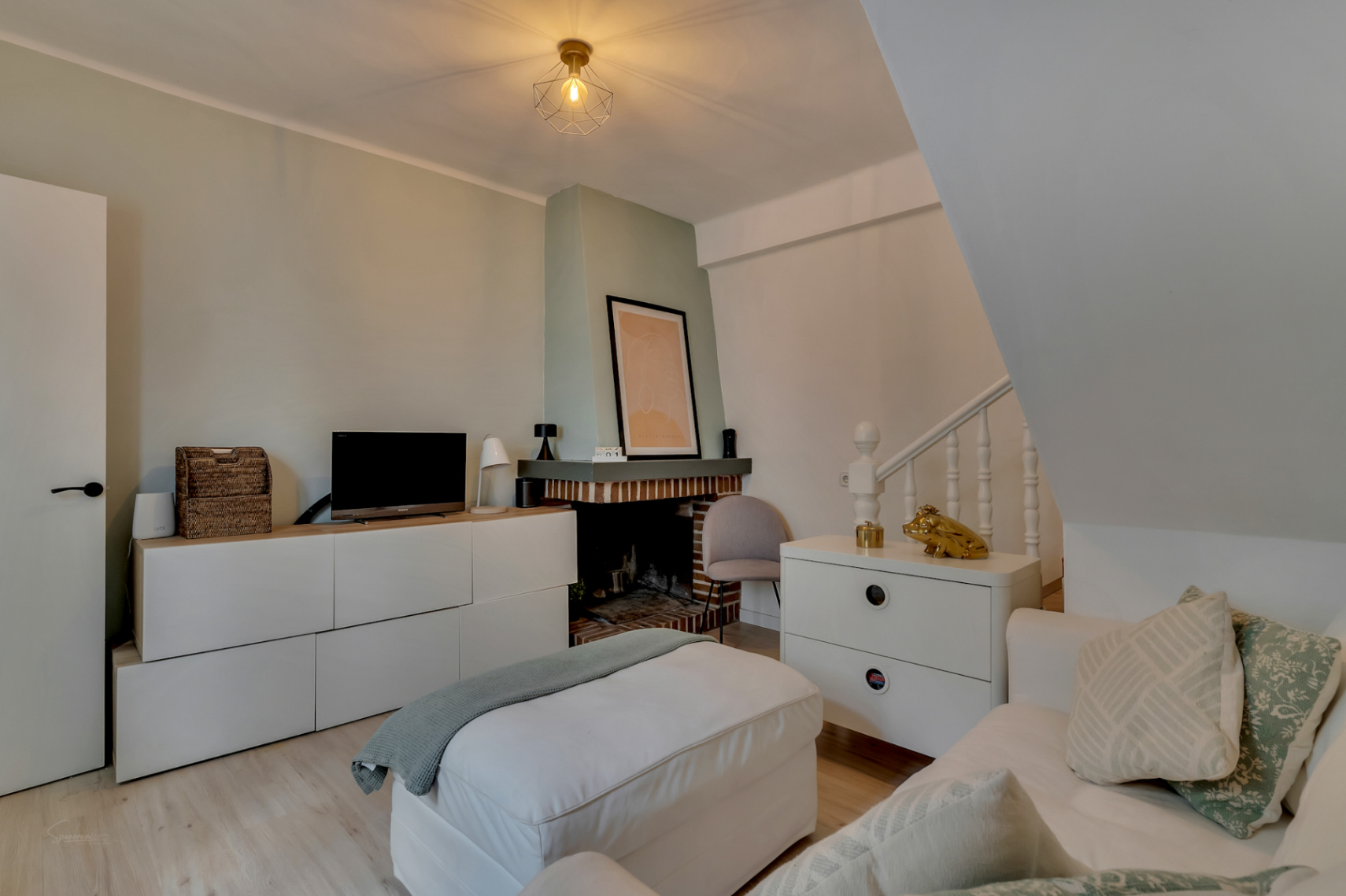 Salon avec cheminée en briques, mobilier blanc et parquet clair.