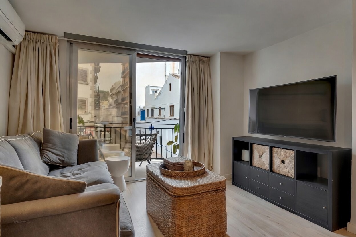 Salon moderne avec canapé gris, meuble TV noir et accès au balcon avec vue urbaine.