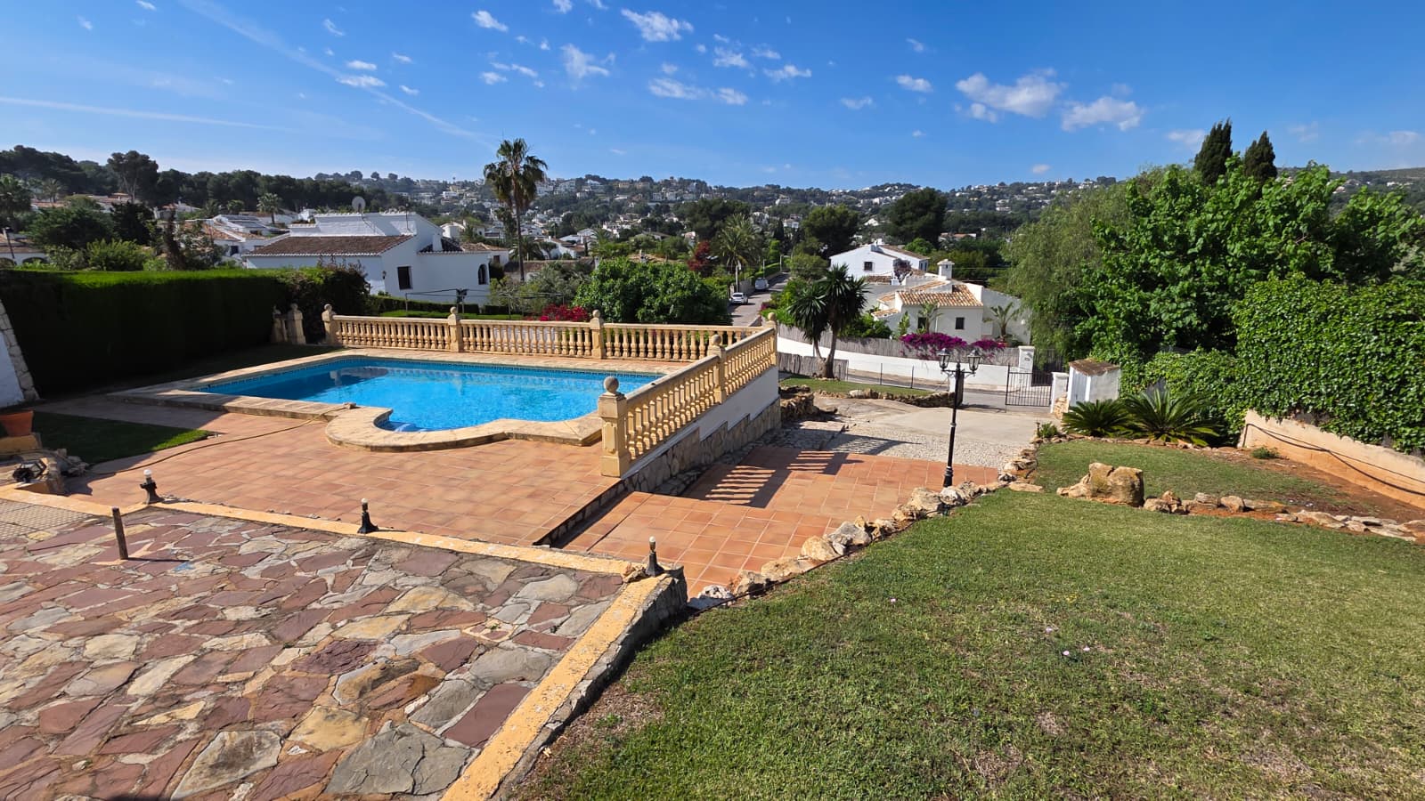 Piscine extérieure avec balustrade classique en pierre, terrasse en terre cuite et vue dégagée sur les collines environnantes de Jávea.