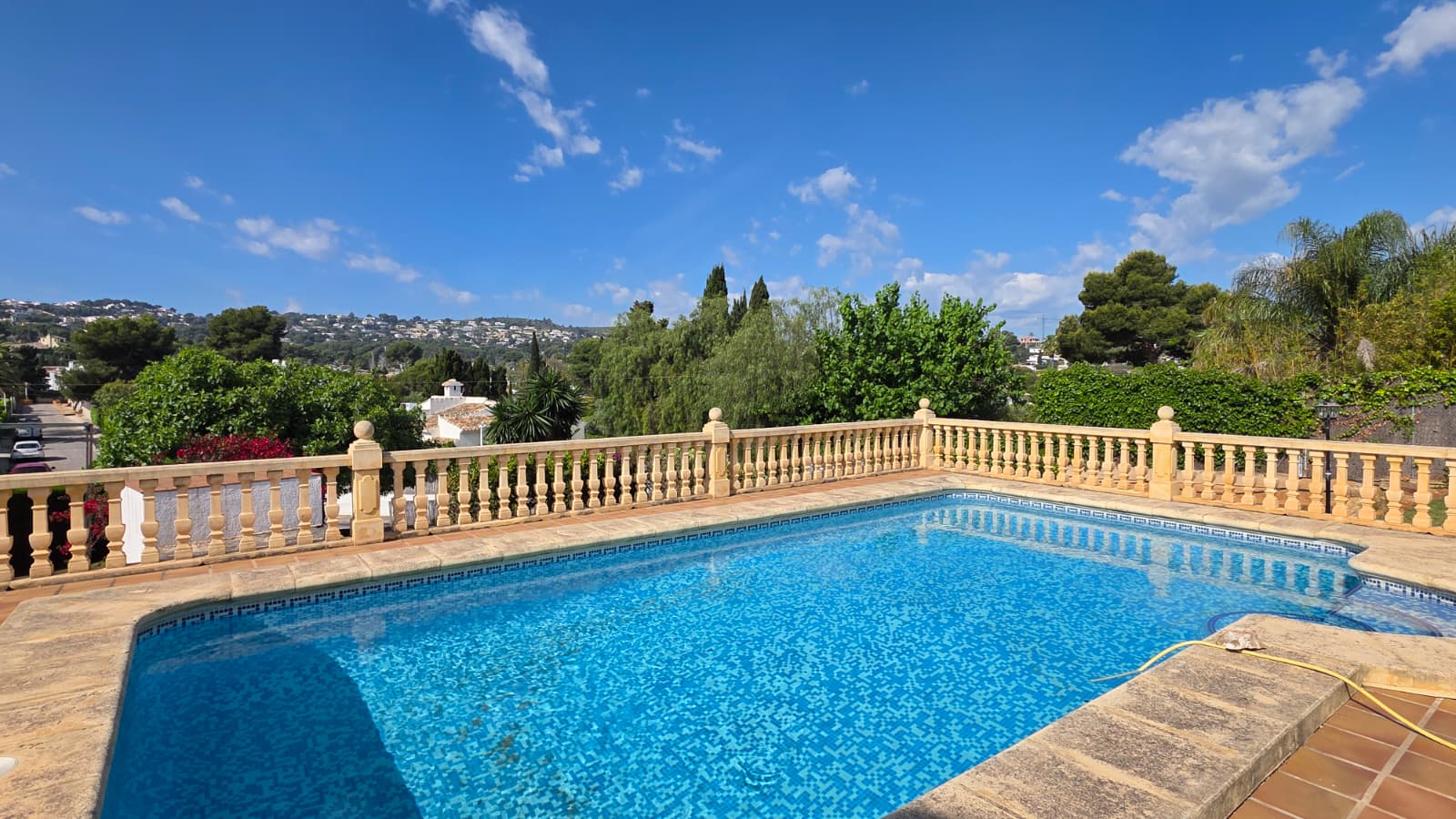 Piscine surélevée avec mosaïque bleue, entourée d'une balustrade en pierre classique offrant une vue panoramique sur les collines environnantes de Jávea.