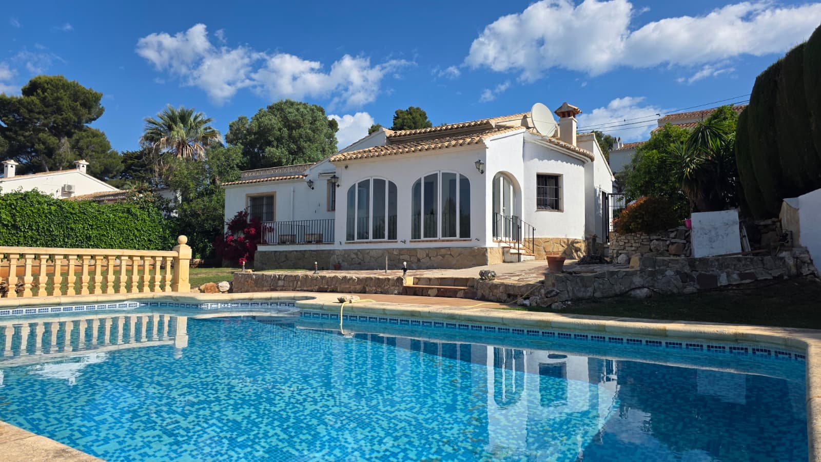 Vue extérieure de la piscine privée et de la villa blanche avec ses fenêtres en arche et son soubassement en pierre naturelle à El Tosalet, Jávea.
