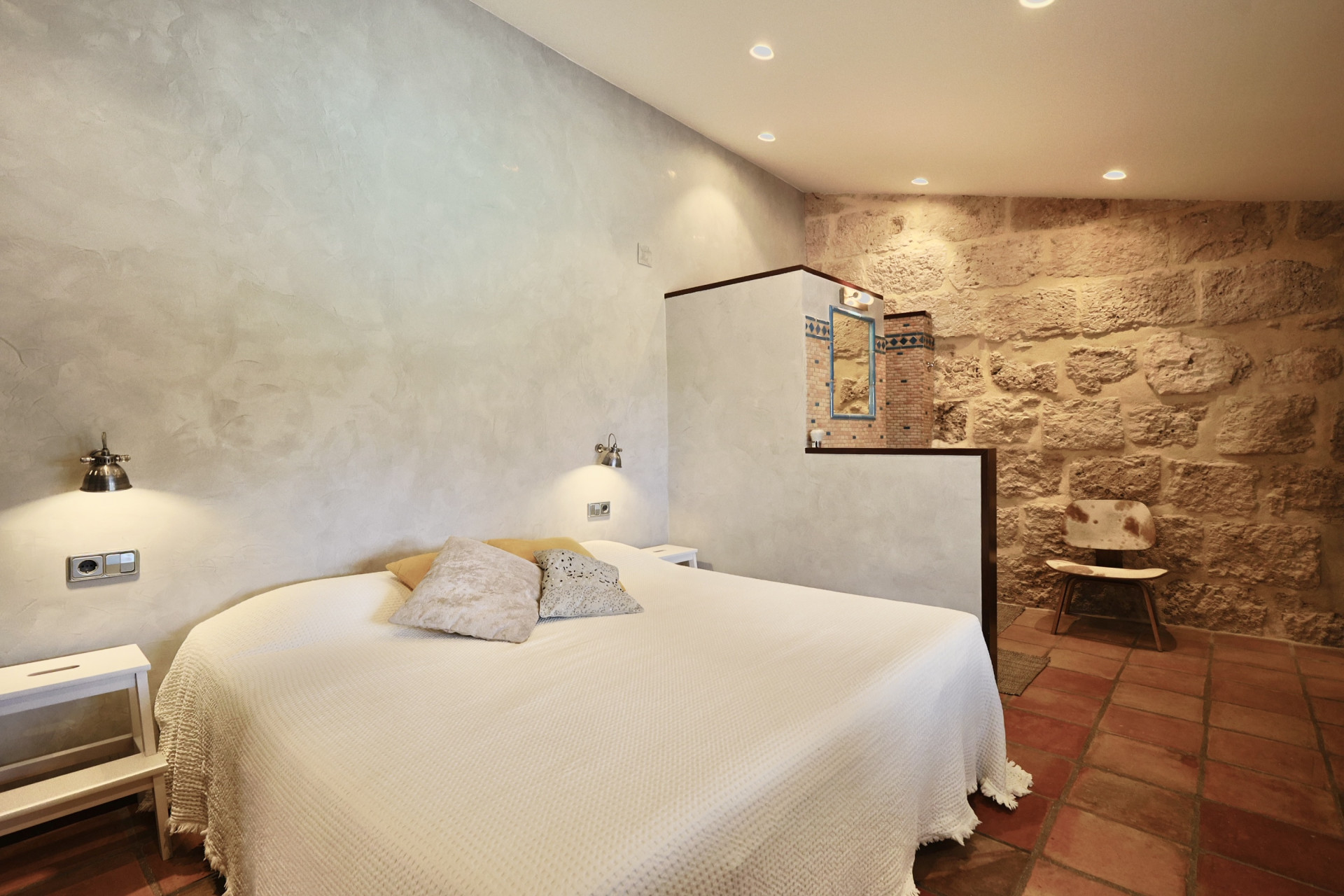 Chambre avec mur en pierre apparente, lit double avec linge blanc et sol en terre cuite.