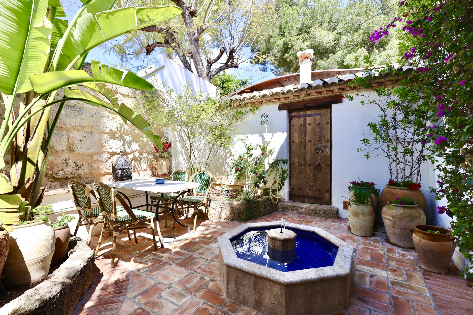Cour intérieure avec fontaine octogonale en mosaïque bleue et coin repas extérieur avec sol en terre cuite.