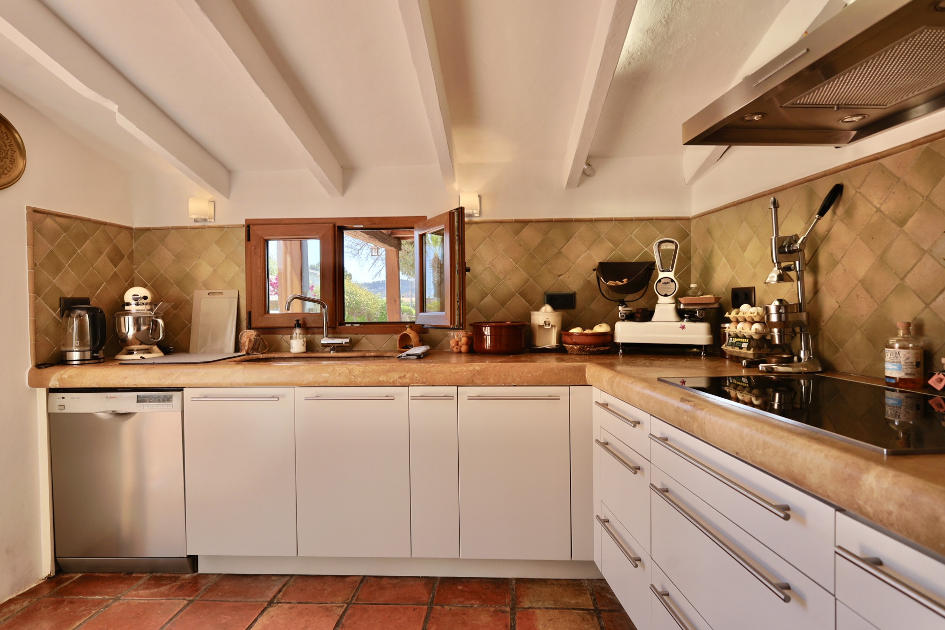 Détail de la cuisine avec comptoir en pierre et carreaux rustiques. Fenêtre en bois avec vue sur l'extérieur.