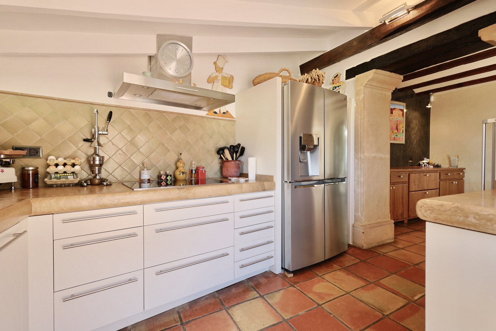 Détail de la cuisine avec un plan de travail en pierre, des carreaux rustiques et un réfrigérateur en inox.