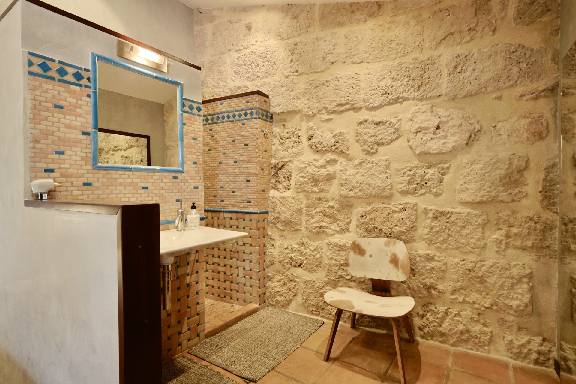 Détail de la salle de bain avec mur en pierre apparente et lavabo avec des carreaux décoratifs.