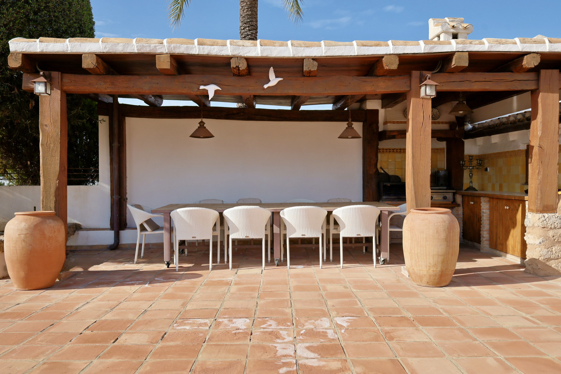 Détail de la terrasse extérieure couverte avec table à manger, chaises en osier et sol en terre cuite.