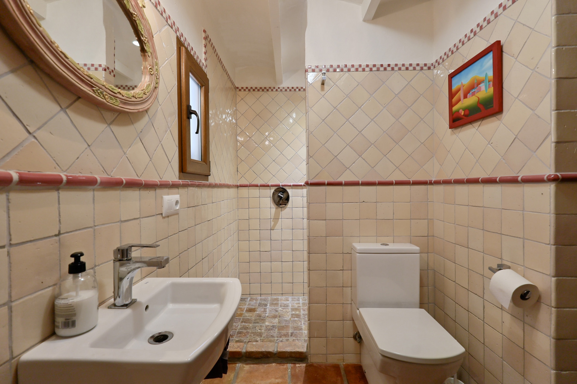 Détail de salle de bain avec carrelage crème, miroir ovale et lavabo blanc dans Villa à Jávea.